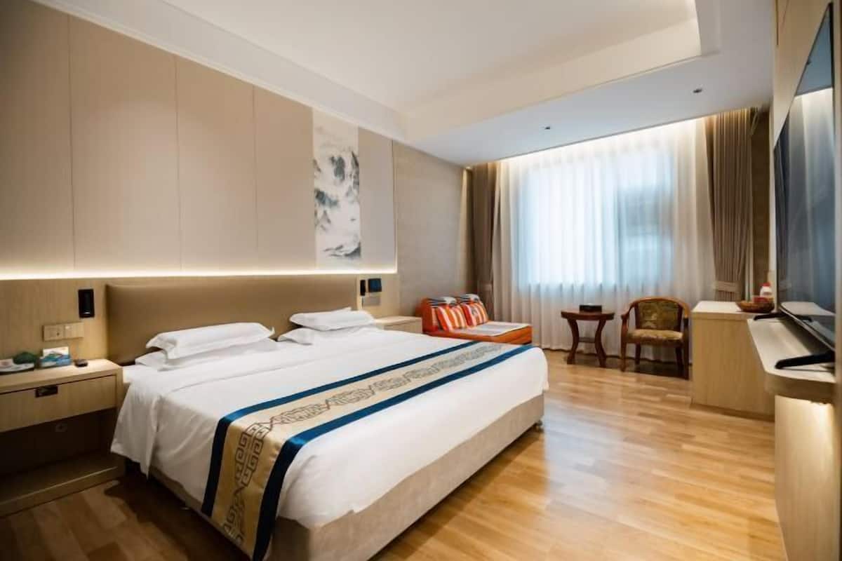 A hotel room with a large bed, a desk, a chair, a TV, and a window with curtains.