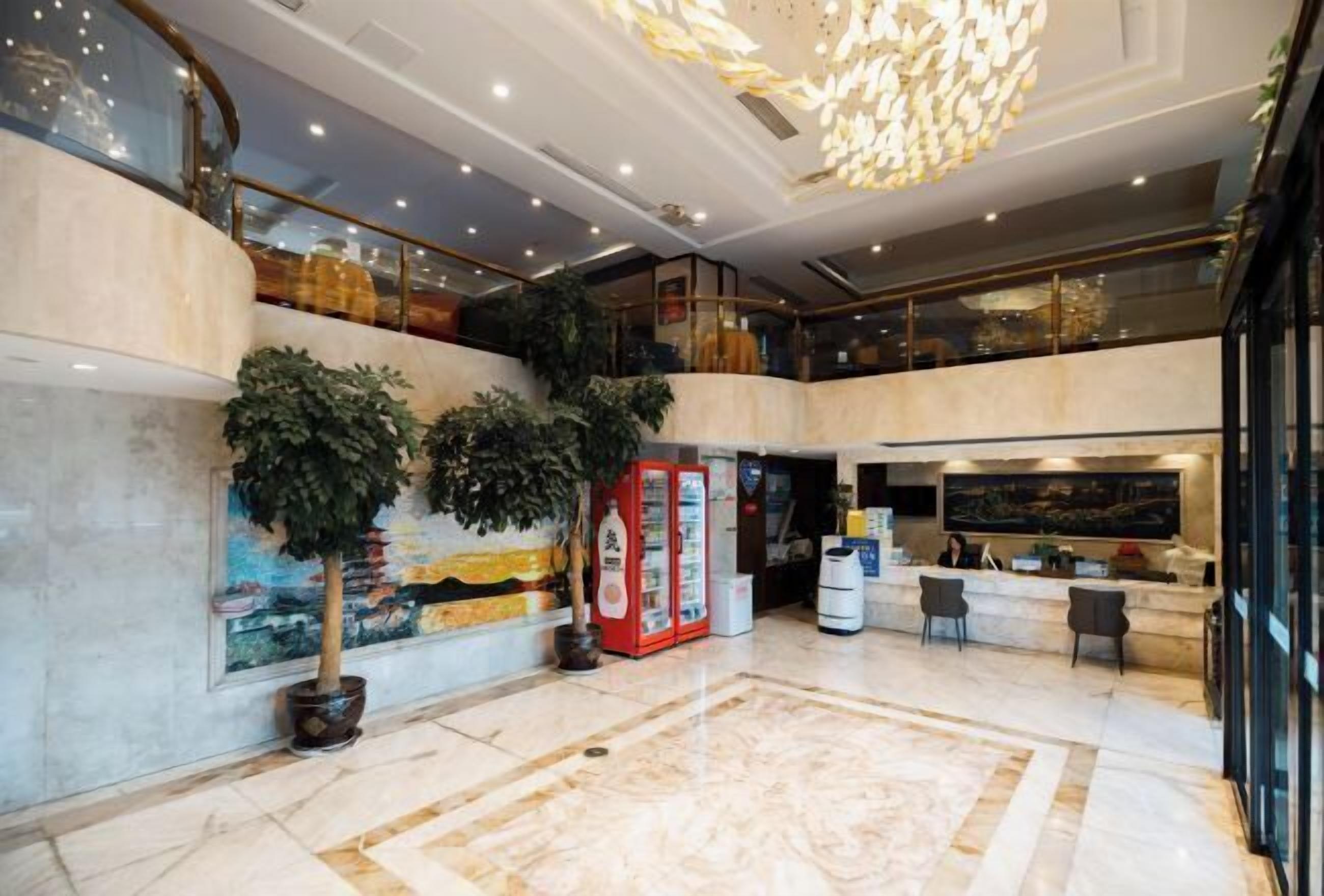 A spacious lobby with a marble floor, a reception desk, and a large chandelier.