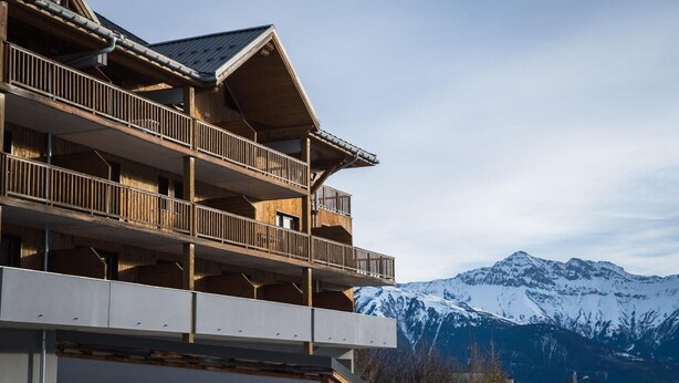 A multi-story building with balconies, set against a backdrop of snow-capped mountains. - Wifi, swimming pool, terrace, balcony, parking, tv, ski locker, 24m², Les Bottières (Saint-Pancrace)