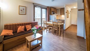 A cozy living area with a sofa, coffee table, and a dining table with chairs. There is a kitchen area in the background with a refrigerator and cabinets. - Wifi, swimming pool, terrace, balcony, parking, tv, ski locker, 24m², Les Bottières (Saint-Pancrace)