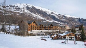 A large wooden lodge with multiple balconies, set against a backdrop of snow-covered mountains. - Wifi, swimming pool, terrace, balcony, parking, tv, ski locker, 24m², Les Bottières (Saint-Pancrace)