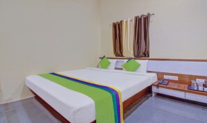 A hotel room with a bed, a bedside table with a phone, and a curtain rod with multiple curtains. - Treebo Shalimar In The Forest (Karjat)