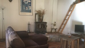 A living room with a sofa, a fireplace, a ladder, a TV, and a framed picture on the wall. - "La Bergerie "Gîte at the end of the world. La Valbonnette (Barrême)