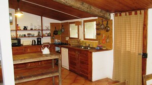 A rustic kitchen with wooden cabinets, a tiled floor, and a hanging pot rack. - "La Bergerie "Gîte at the end of the world. La Valbonnette (Barrême)