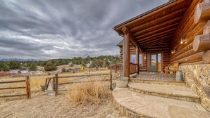 Eine rustikale Holzhütte mit einer Steintreppe, die zu einer Veranda führt, umgeben von trockenem Gras und einem Holzzaun.