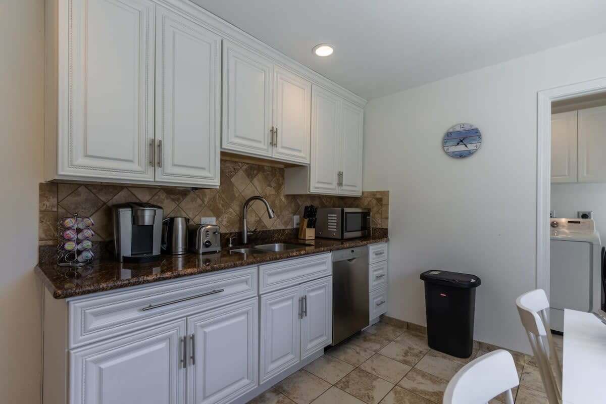 A kitchen with white cabinets, a microwave, a coffee maker, and a trash bin.
