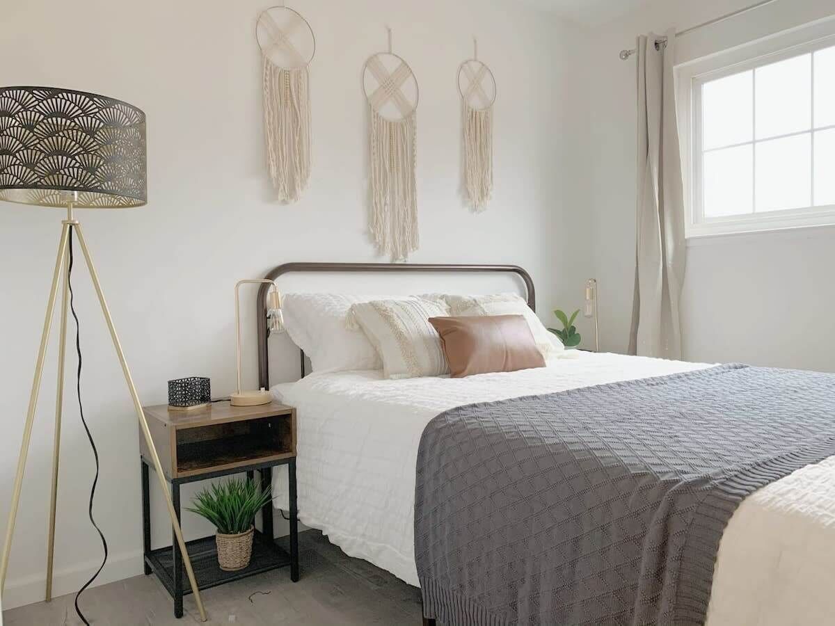 A bedroom with a bed, bedside table, lamp, wall decor, and a window.