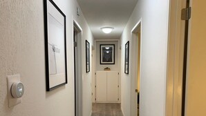 Un pasillo estrecho con una puerta al final, un interruptor de luz a la izquierda y cuadros en las paredes.