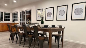 Un comedor con una mesa y sillas de madera, una obra de arte enmarcada en la pared y una cocina al fondo.