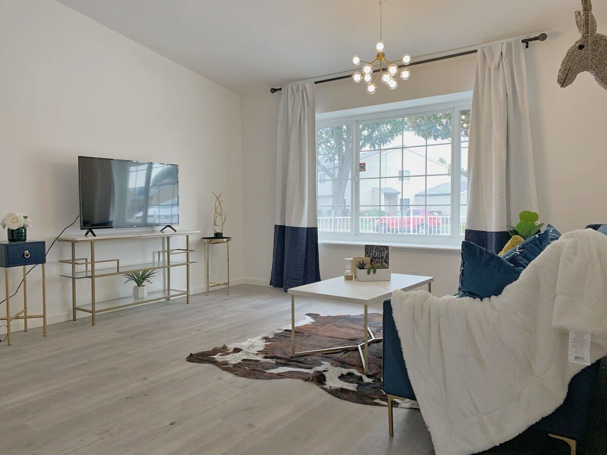 A modern living room with a flat-screen TV, a white coffee table, a blue sofa, and a cowhide rug.