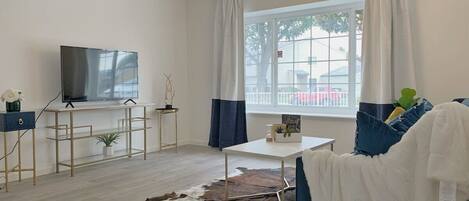 A modern living room with a flat-screen TV, a white coffee table, a blue sofa, and a cowhide rug.