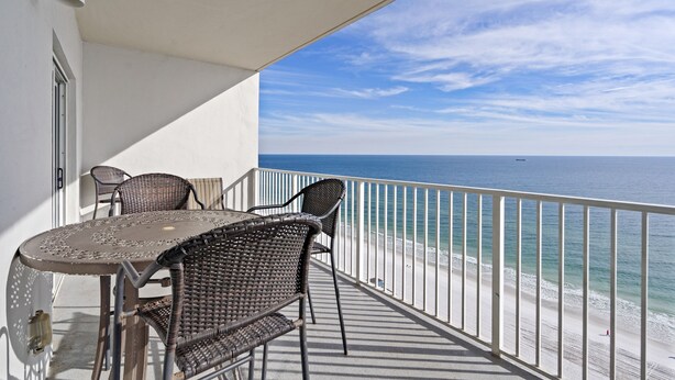 A balcony with a table and chairs, overlooking a beach and the ocean. - Seawind 1705 by Liquid Life (Gulf Shores)