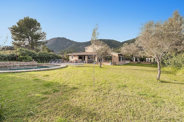 Uma casa com piscina, cercada por gramado e árvores, com montanhas ao fundo.