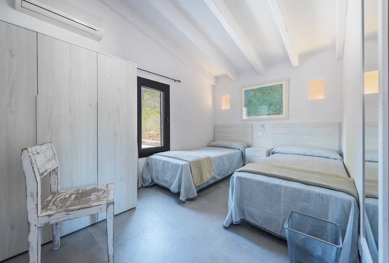 Une chambre avec deux lits simples, une chaise en bois, une fenêtre et un climatiseur fixé au mur.