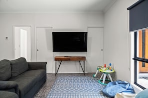 A living room with a grey sofa, a wooden coffee table, a flat-screen TV mounted on the wall, and a patterned rug on the floor.