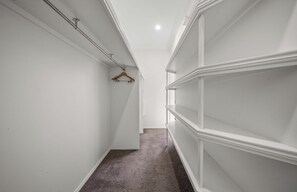 A narrow hallway with white walls and a carpeted floor, leading to a room with built-in shelving.