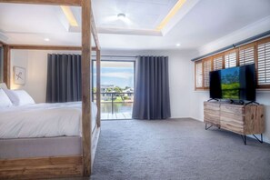 Quarto com cama, televisão, penteadeira de madeira e varanda com cortinas.