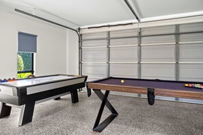 Ein Billardtisch mit Spielzeug und Kugeln, ein Kicker und ein Fenster mit Blick auf Grünflächen.