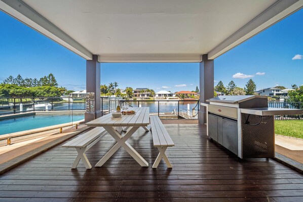 Un patio exterior con piscina, bancos de madera y una parrilla.