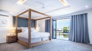 Une chambre à coucher avec un lit à baldaquin, une table de chevet, une fenêtre avec des rideaux et une vue sur l’extérieur.