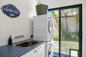 A laundry room with a sink, a bottle of hand soap, and a self-service sign.