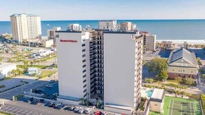 A high-rise hotel with a view of the beach, a parking lot, and a tennis court. - Wonderful oceanview condo, 3 bedrms, near the beach (Myrtle Beach)