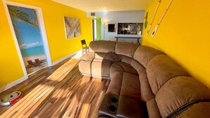 A living room with a sectional sofa, wooden flooring, and a view of the beach through a door. - Wonderful oceanview condo, 3 bedrms, near the beach (Myrtle Beach)