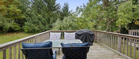 Une terrasse en bois avec une table et des chaises, entourée d’arbres.
