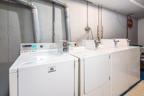 Un área de lavandería con varias lavadoras blancas, un panel de control y tuberías visibles en la pared.