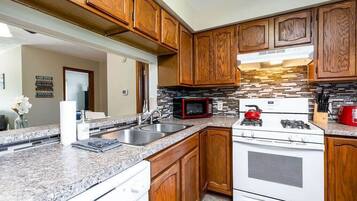 Una cocina con armarios de madera, encimeras de granito, estufa, microondas y pileta.