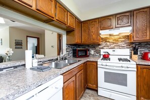 Una cocina con armarios de madera, encimeras de granito, estufa, microondas y pileta.