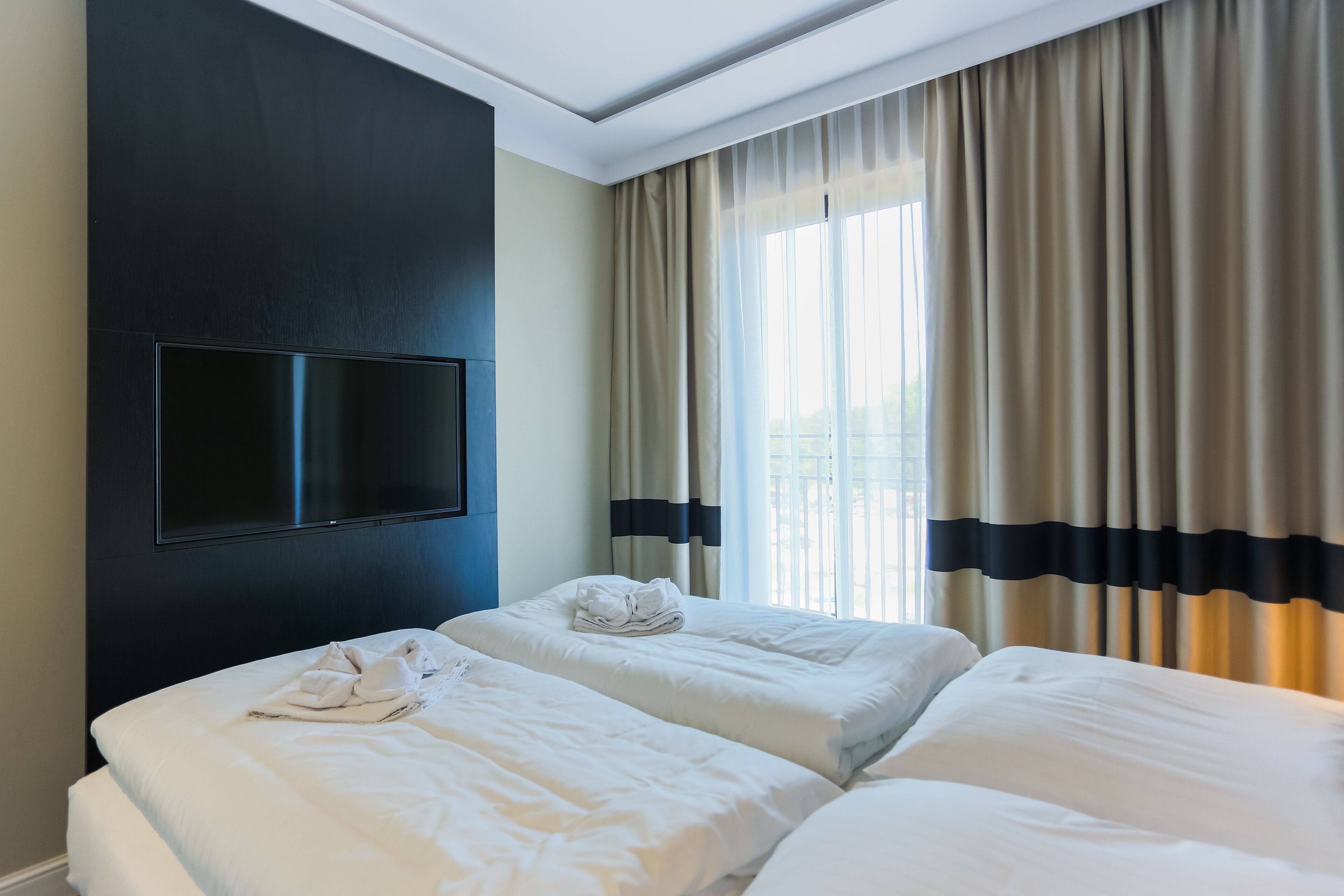 A hotel room with two beds, a flat-screen TV mounted on the wall, and a large window with curtains.