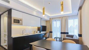 Een moderne hotelkamer met een kitchenette, een eetgedeelte en een zithoek met een bank en stoelen.