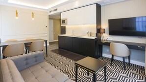Een moderne hotelkamer met een bank, eettafel, stoelen, een kitchenette en een televisie.