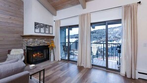 Ein geräumiges Wohnzimmer mit Kamin, einer Couch und Blick auf eine verschneite Landschaft durch große Schiebeglastüren.