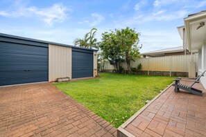 A backyard with a grassy lawn, a brick patio, and a metal garage door.