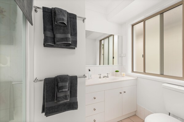 A bathroom with a glass shower door, a white sink with a mirror above it, and a toilet. There are two towels hanging on a towel rack.