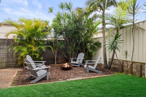 Un giardino sul retro con un braciere, due poltrone Adirondack e diverse piante tropicali.
