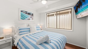 Un dormitorio con cama, mesita de noche, lámpara, un cuadro enmarcado y una ventana con persianas.