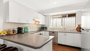 Una cocina moderna con armarios blancos, encimera de granito, microondas, lavavajillas y una ventana con vistas al exterior.