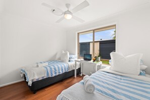 A bedroom with two beds, a desk, and a ceiling fan.