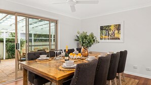 Un comedor con una mesa de madera, sillas tapizadas de color negro y un separador de vidrio que divide el comedor de un jardín.