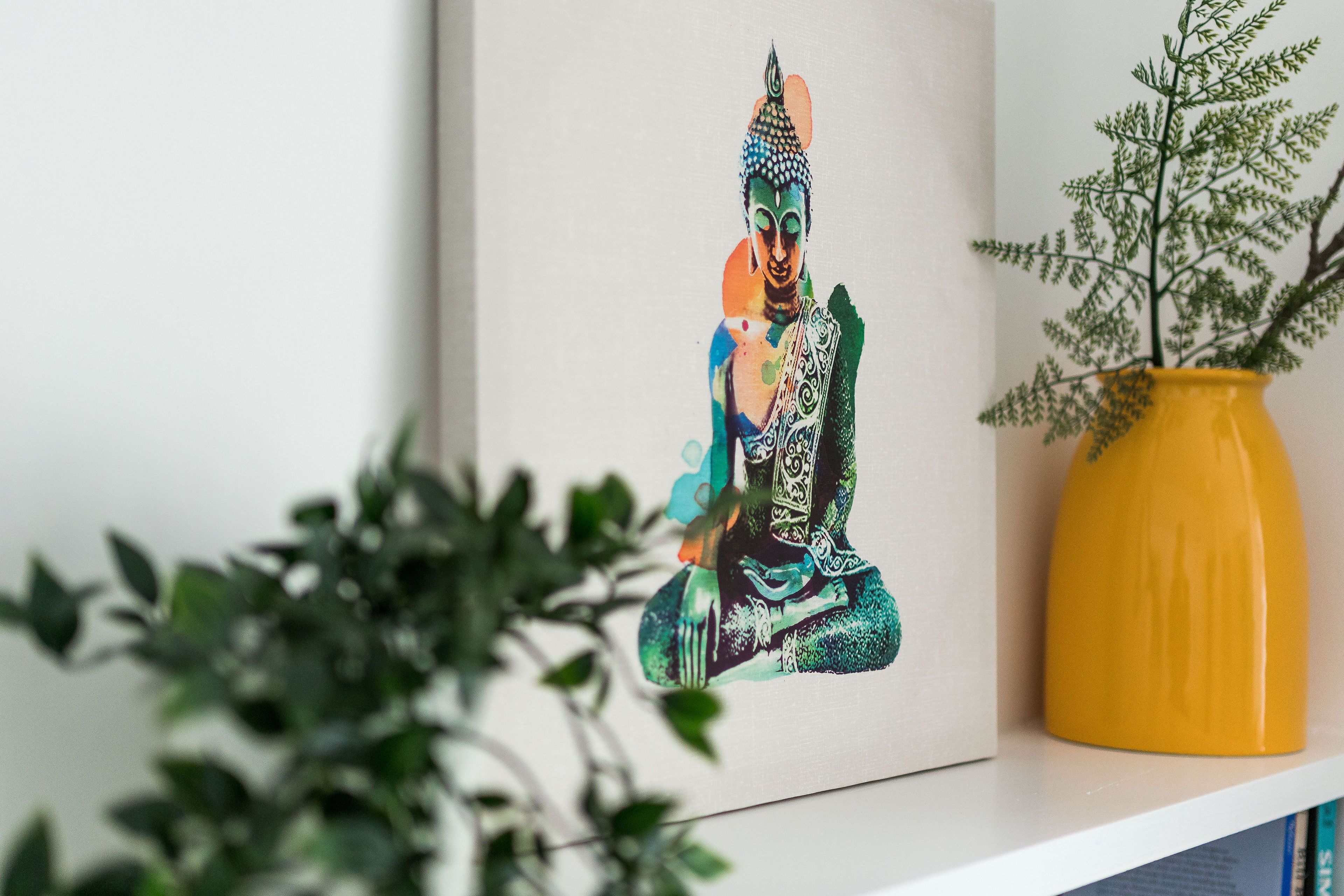 Una obra de arte enmarco con la imagen de una figura sentada en un estante, junto a un jarrón amarillo con una planta.