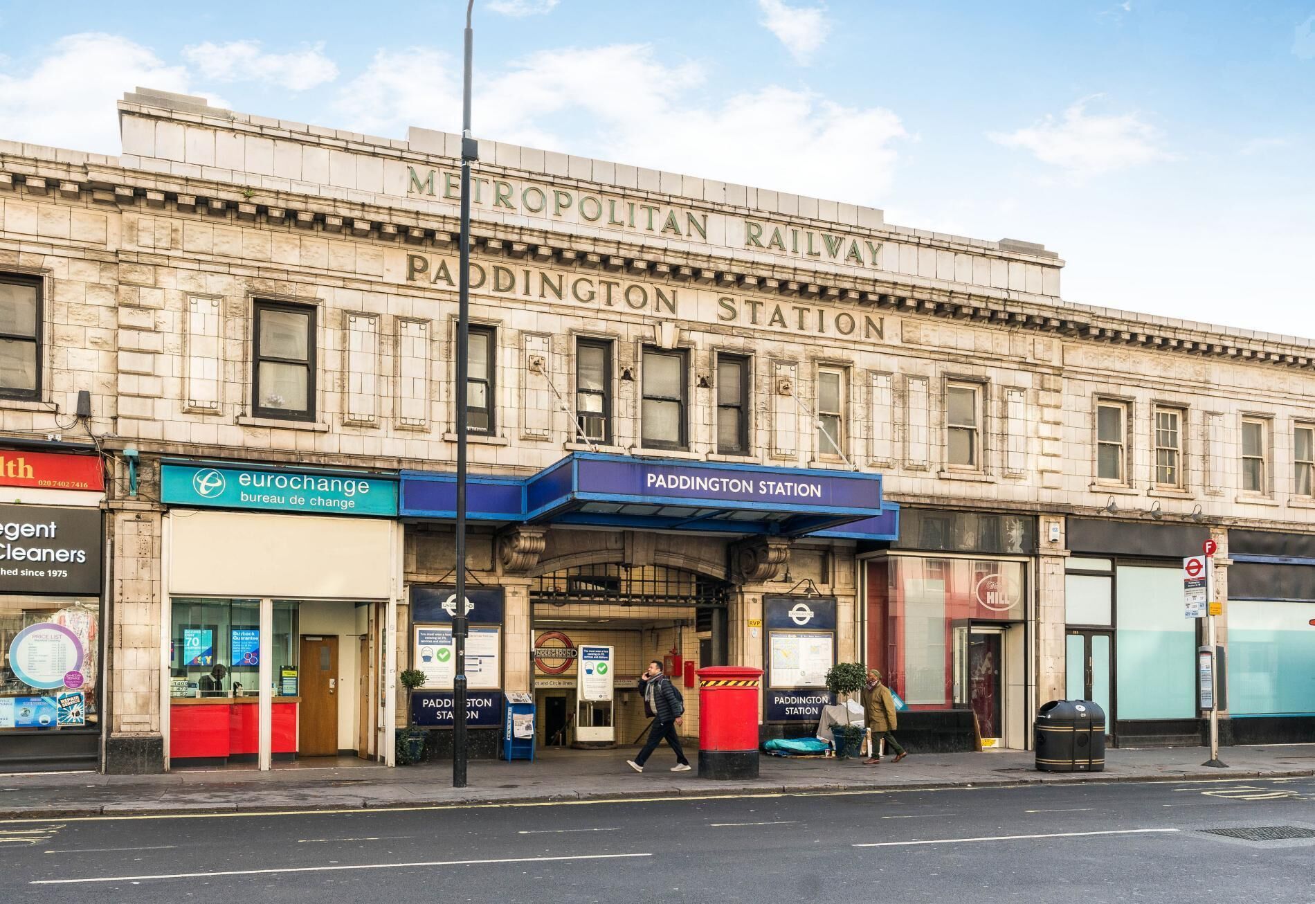 Estación Paddington, con un letrero de la línea de metro Metropolitan, una casa de cambio Eurochange y un bote de basura rojo.