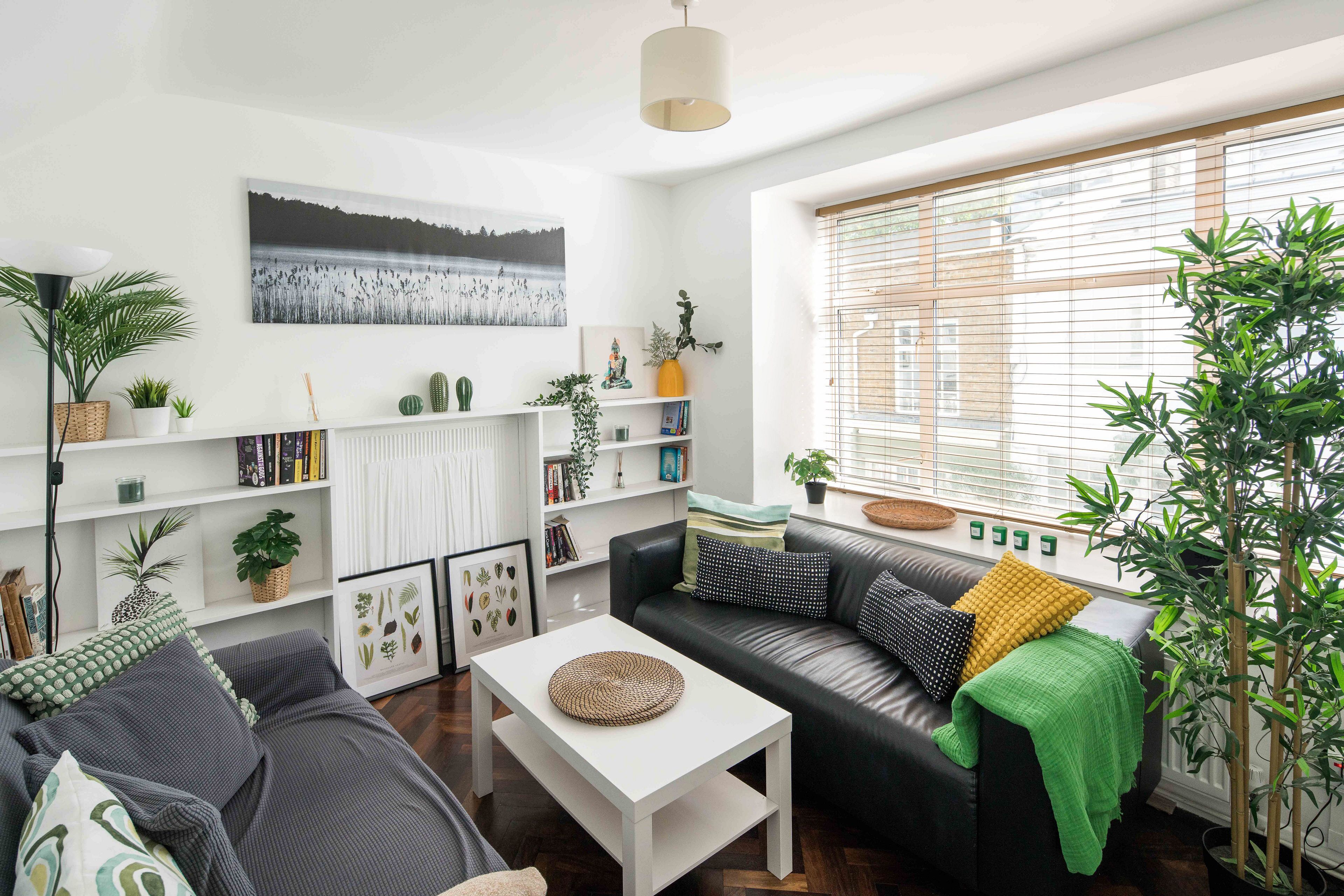 Una sala moderna con un sofá de cuero negro, una mesa de centro blanca y una estantería llena de libros y objetos decorativos.