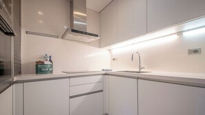Eine moderne Küche mit weißen Schränken, einer Edelstahl-Dunstabzugshaube, einer integrierten Spüle und einer Arbeitsplatte mit einer Wasserflasche und einer Packung Toilettenartikeln.
