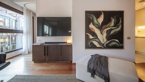 Ein modernes Wohnzimmer mit einem großen Flachbildfernseher, einem schlichten Schrank und einem großformatigen abstrakten Gemälde an der Wand.