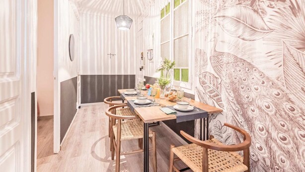 Uma sala de jantar com uma mesa comprida, cadeiras e um papel de parede com tema de pavão.