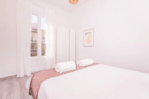A bedroom with a bed, a window with curtains, a framed picture on the wall, and a balcony view.