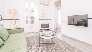 Uma sala de estar moderna com um sofá verde, uma mesa de centro redonda com revistas, um abajur e uma TV fixada na parede.